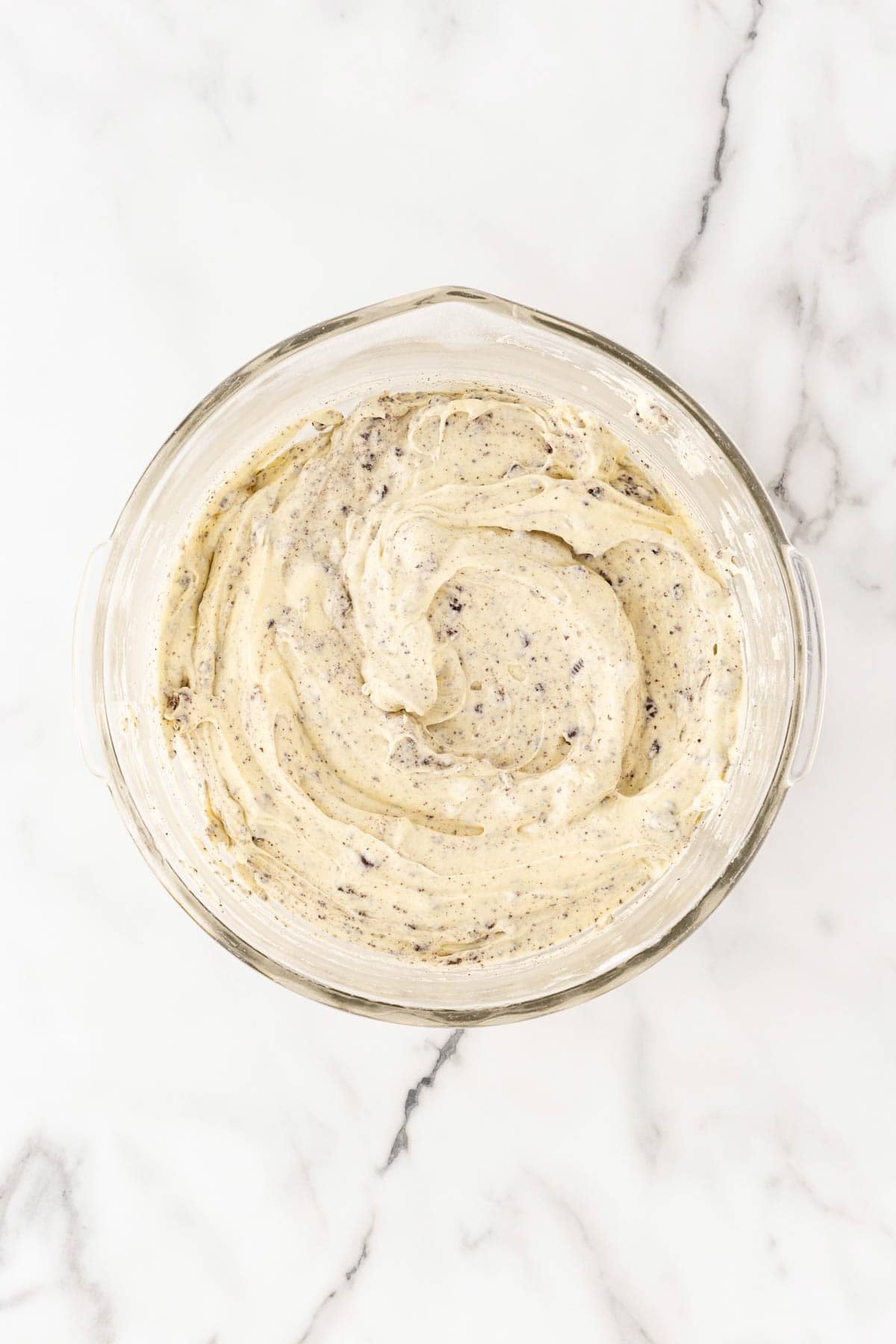Oreo pound cake batter with crushed cookie pieces mixed in a glass bowl
