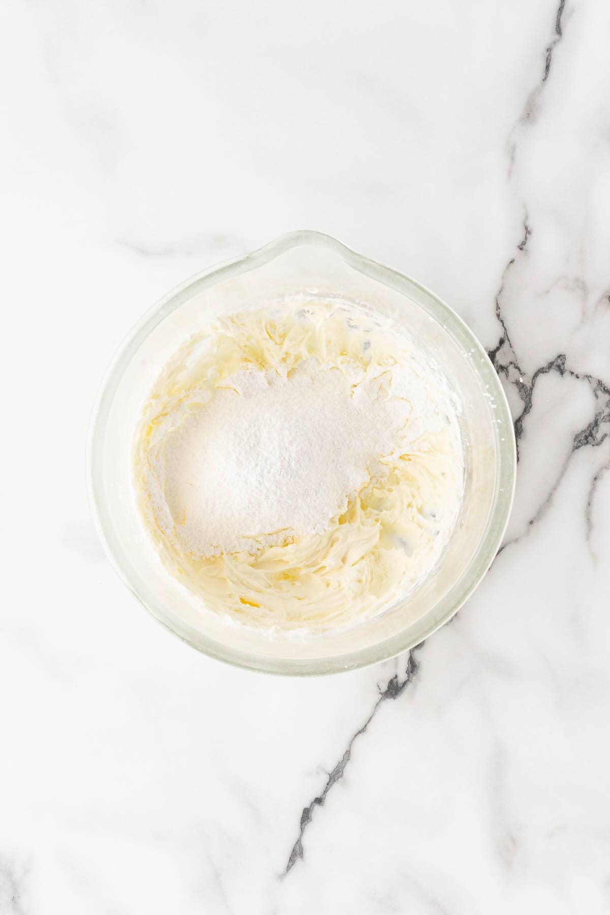 Powdered sugar added to a bowl of softened cream cheese for glaze preparation