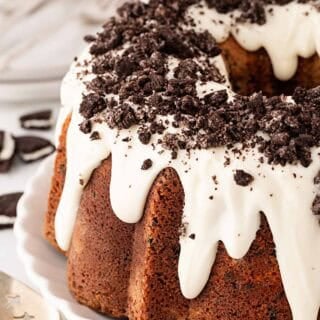 Closeup of Oreo pound cake with white glaze dripping down the sides and crushed chocolate sandwich cookies sprinkled on top