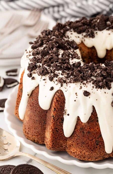 Closeup of Oreo pound cake with white glaze dripping down the sides and crushed chocolate sandwich cookies sprinkled on top