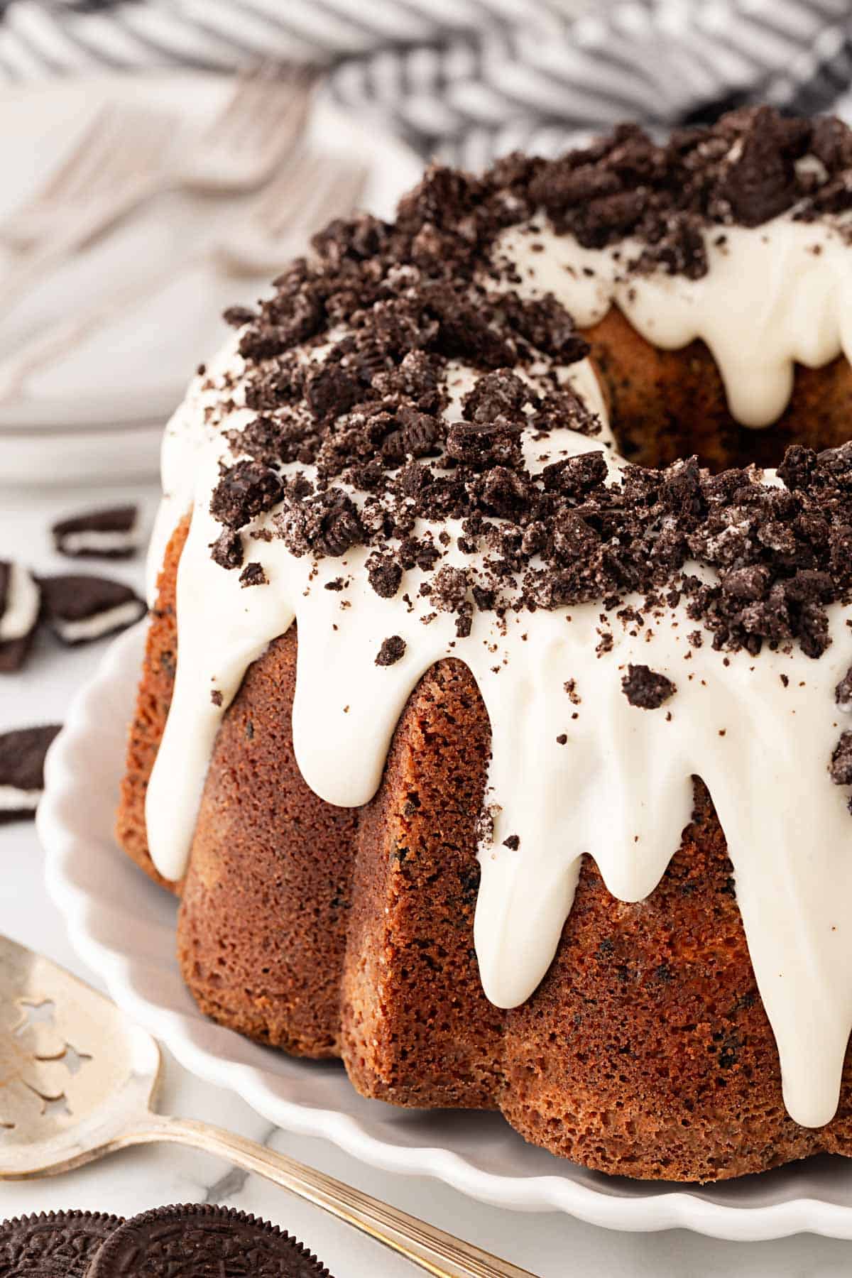 Closeup of Oreo pound cake with white glaze dripping down the sides and crushed chocolate sandwich cookies sprinkled on top