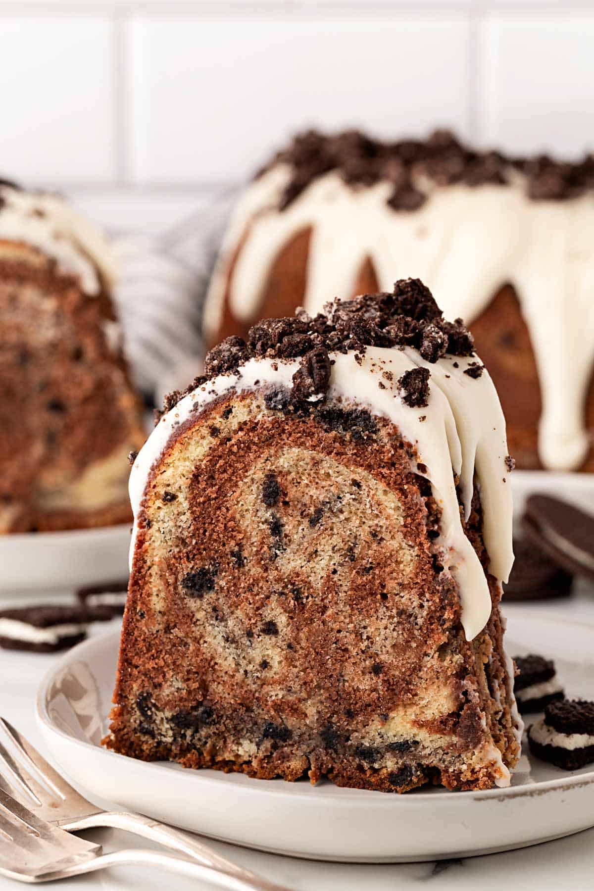 Slice of Oreo pound cake showing chocolate and vanilla swirl with cookie pieces inside, topped with glaze and cookie crumbs