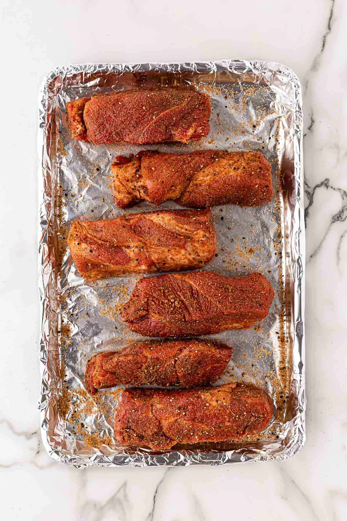 Pork ribs coated evenly with dry rub on a foil-lined baking sheet