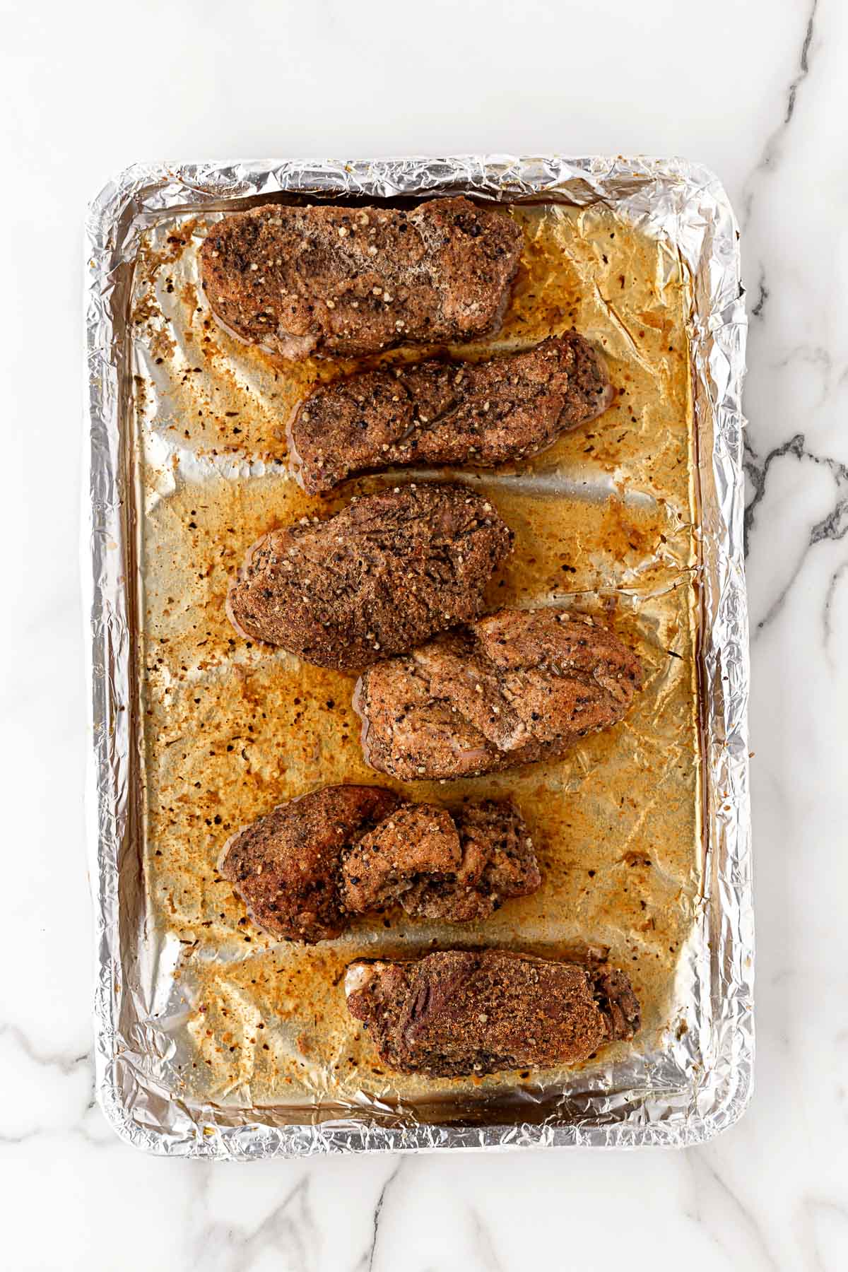 Baked pork ribs with browned seasoning on a foil-lined baking sheet