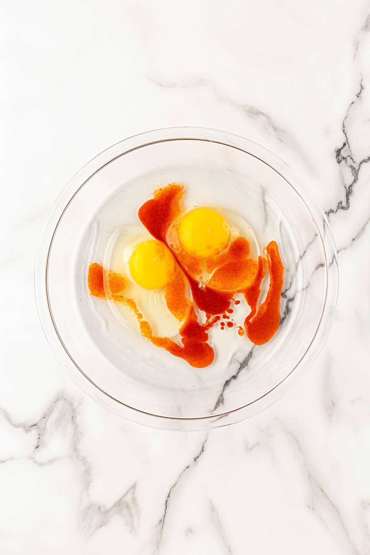 Two eggs with hot sauce in a glass bowl for an egg wash