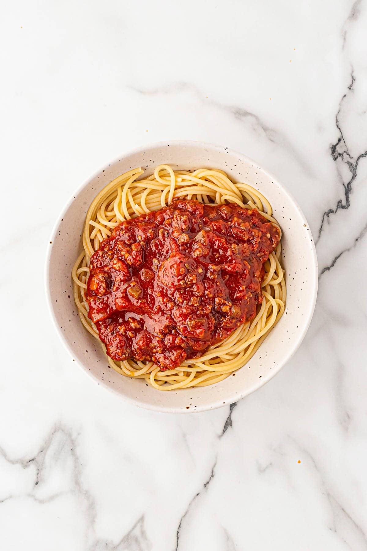 Bowl of spaghetti topped with hearty meat sauce on a marble surface