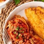 Closeup of spaghetti with meat sauce and a crispy fried fish fillet on a plate