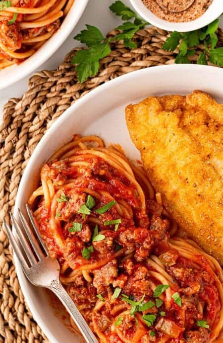 Closeup of spaghetti with meat sauce and a crispy fried fish fillet on a plate