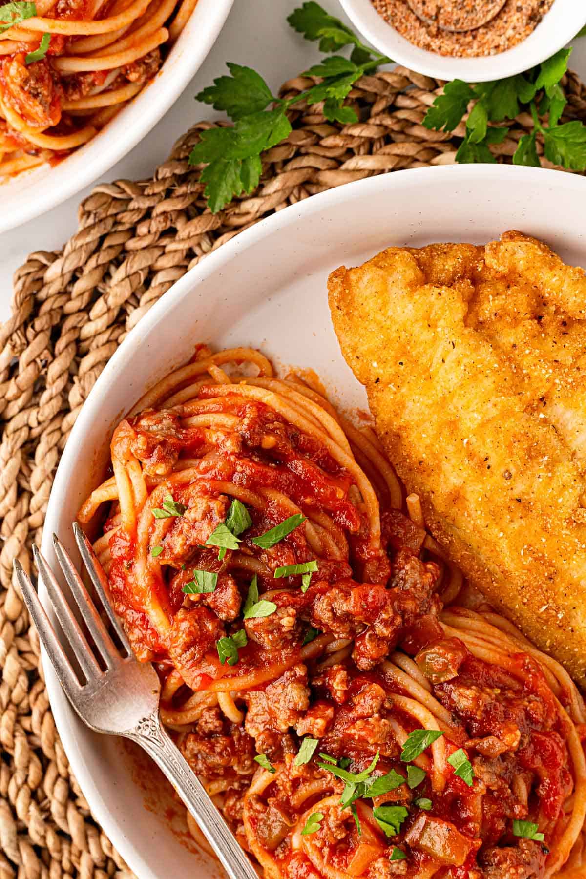 Closeup of spaghetti with meat sauce and a crispy fried fish fillet on a plate