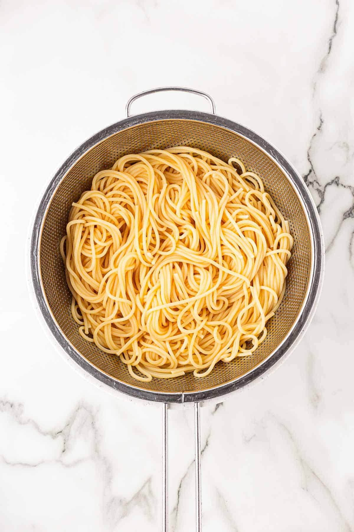 Cooked spaghetti noodles draining in a metal colander