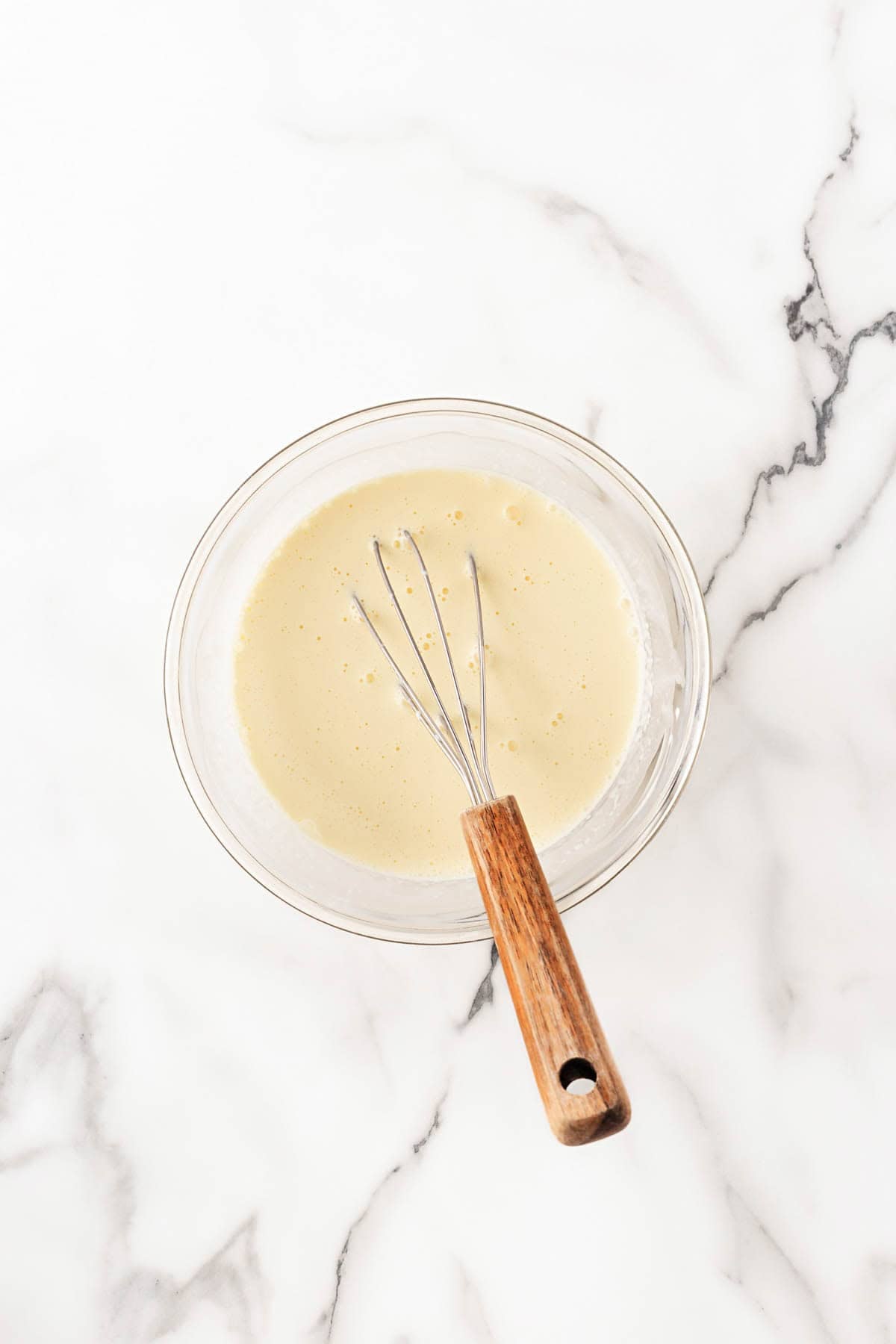 Wet ingredients whisked together in a glass bowl on a marble surface