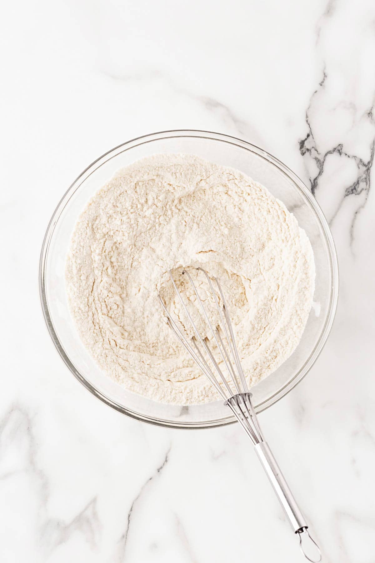 Dry ingredients in a bowl with a whisk on a marble countertop