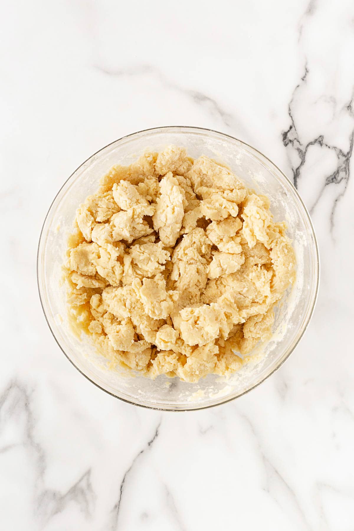 Dough mixture forming into soft, shaggy clumps in a bowl