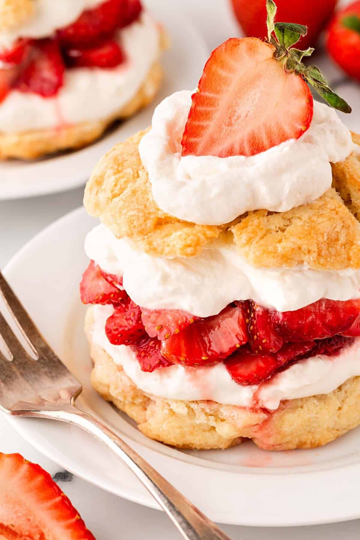 Strawberry shortcake topped with whipped cream and a fresh strawberry, served on a plate with a fork nearby
