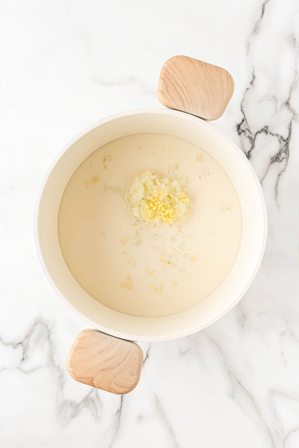 Bowl of milk and chicken stock with minced garlic and onion added in the center