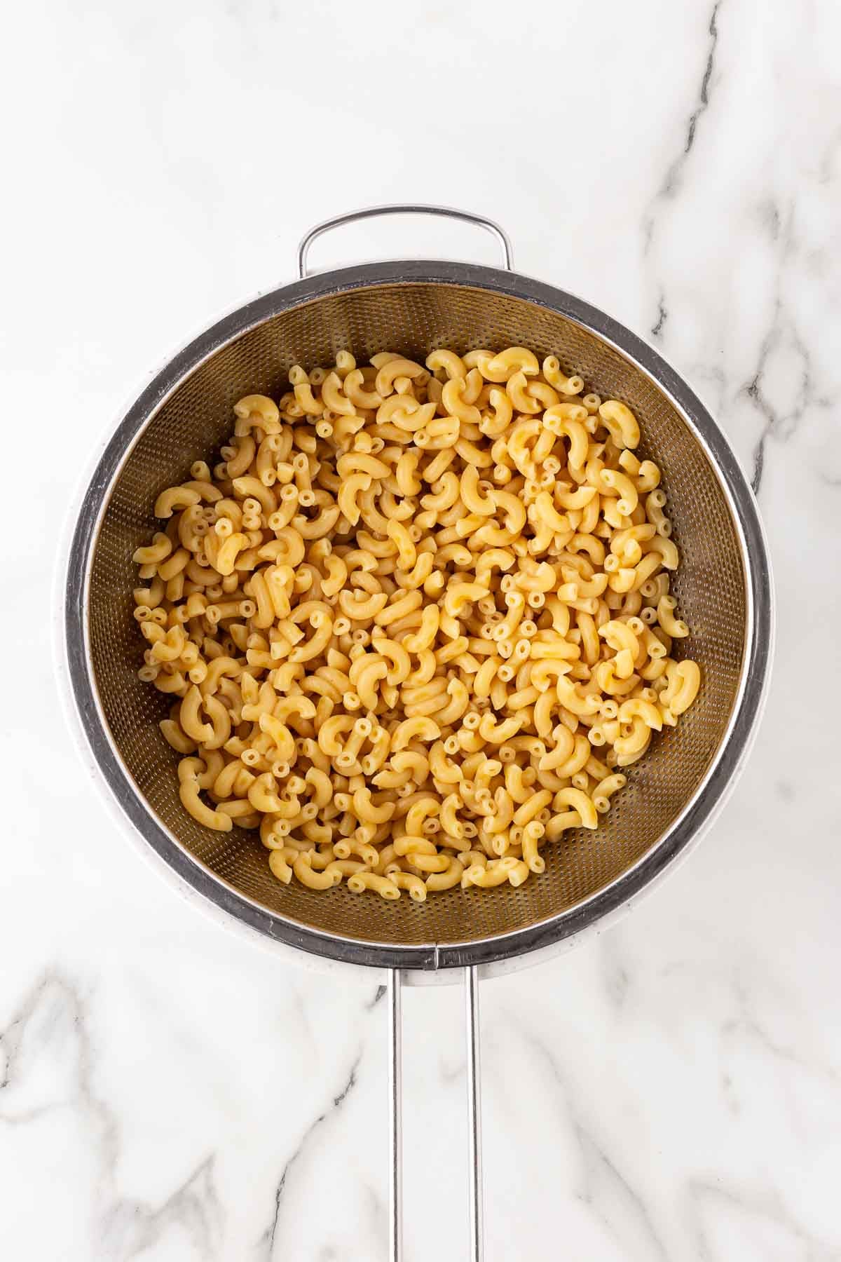 Cooked elbow macaroni draining in a metal colander