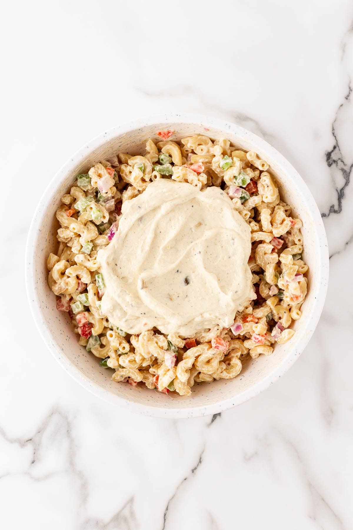 Macaroni salad mixture in bowl with extra dressing added on top