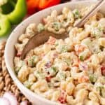 Closeup of creamy macaroni salad with diced vegetables, with a spoon in it