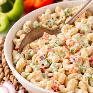 Closeup of creamy macaroni salad with diced vegetables, with a spoon in it