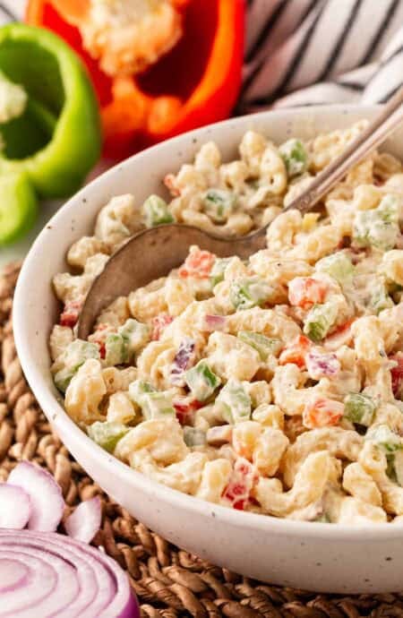 Closeup of creamy macaroni salad with diced vegetables, with a spoon in it