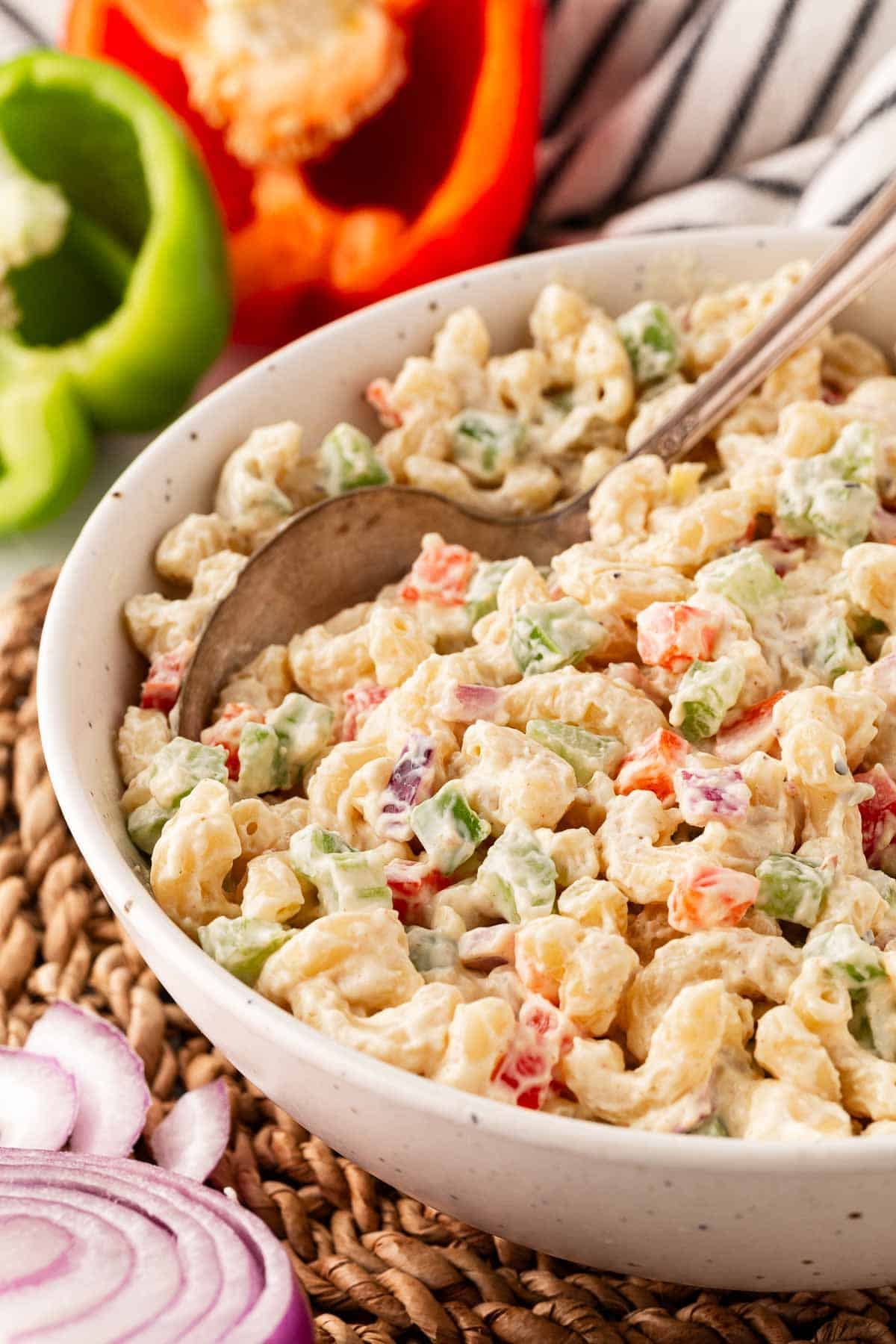 Closeup of creamy macaroni salad with diced vegetables, with a spoon in it
