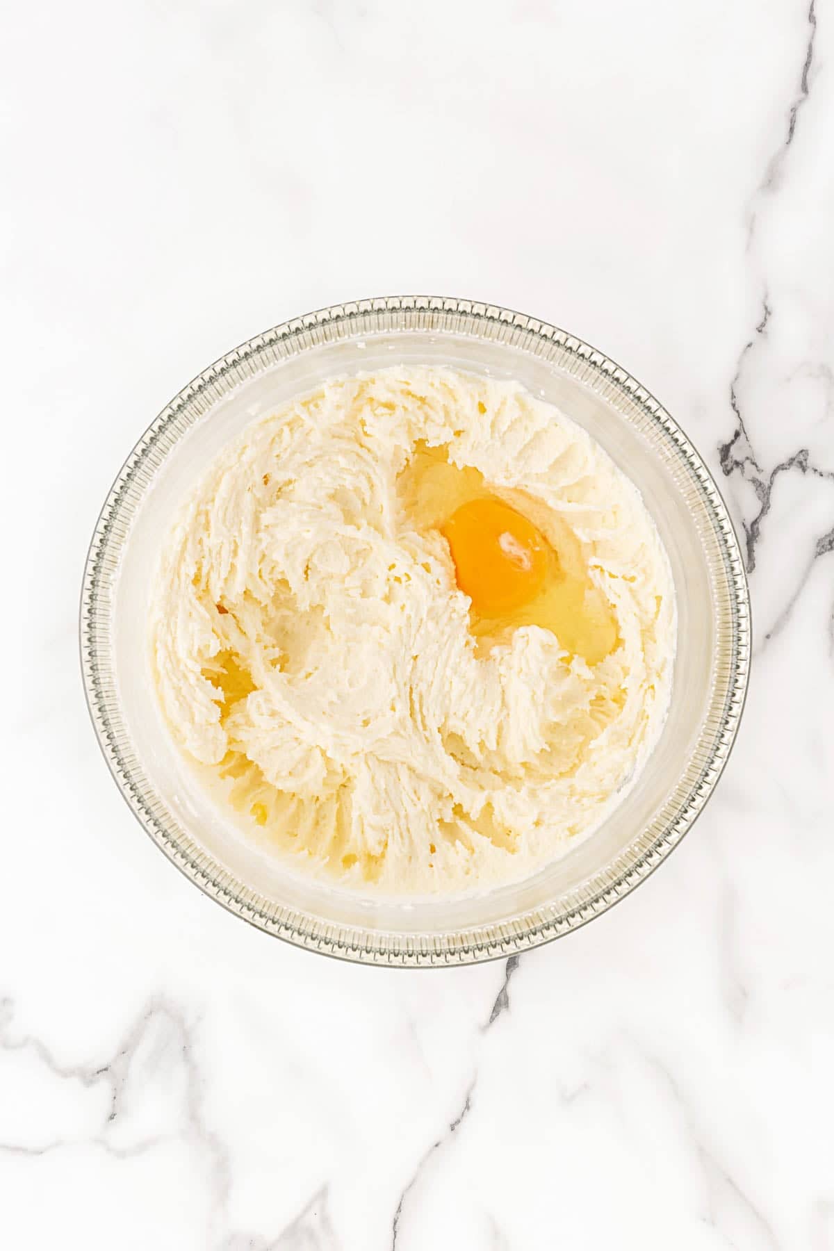 Creamed butter and sugar mixture with an egg in a mixing bowl for pound cake batter