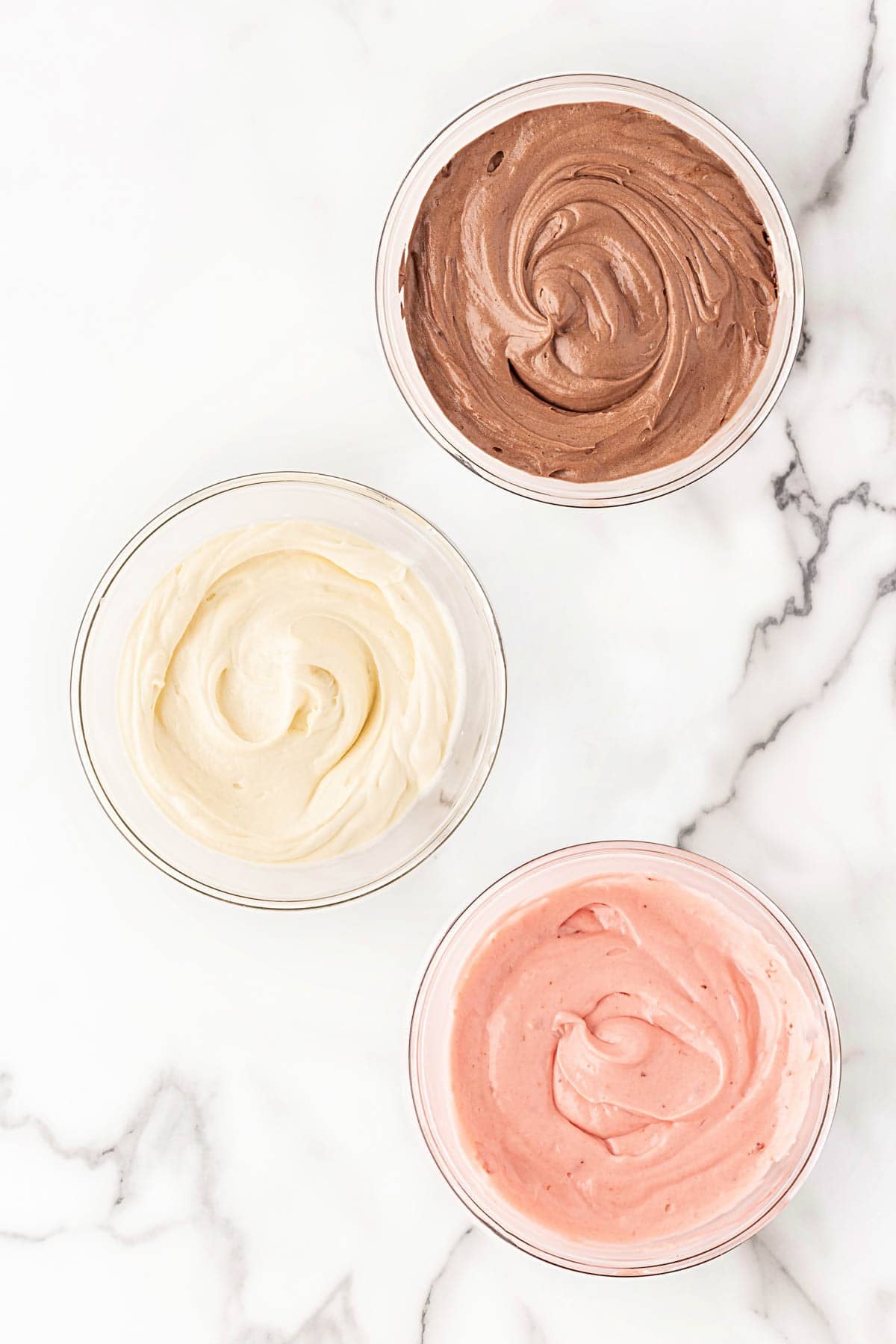 Three bowls of Neapolitan pound cake batter in vanilla, chocolate, and strawberry flavors
