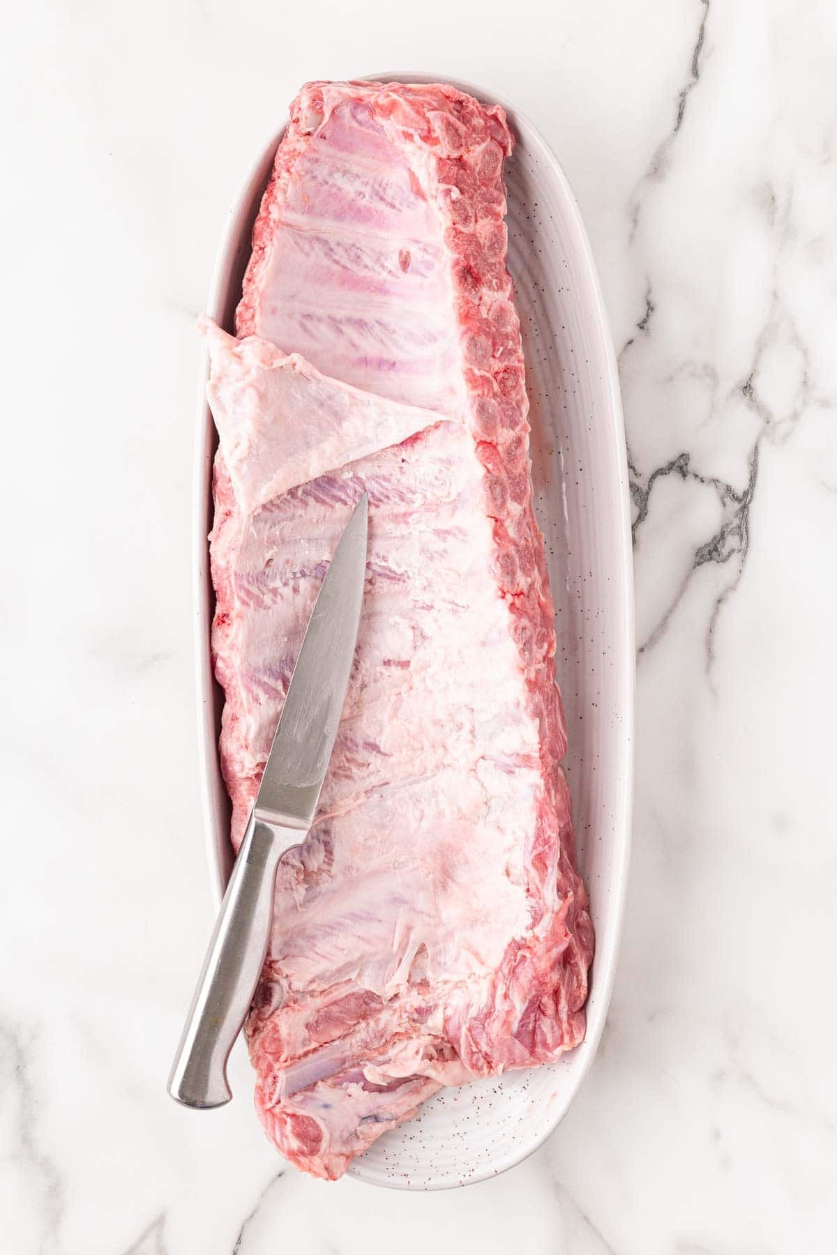 Removing the membrane from a rack of raw pork ribs with a knife