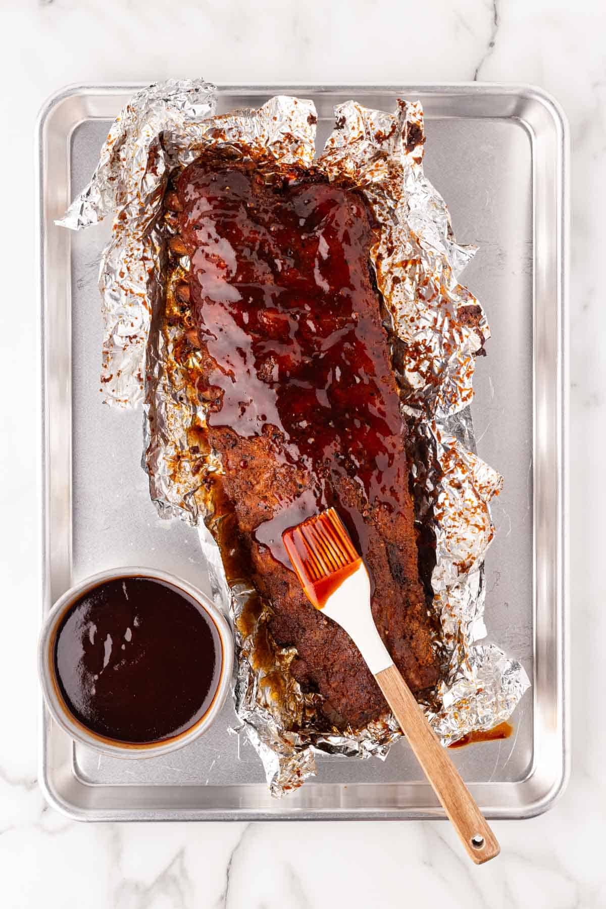 BBQ sauce brushed over baked ribs on an open foil-lined tray