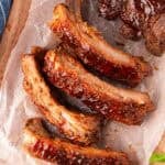 Overhead shot of oven baked ribs sliced and brushed with sauce on parchment paper