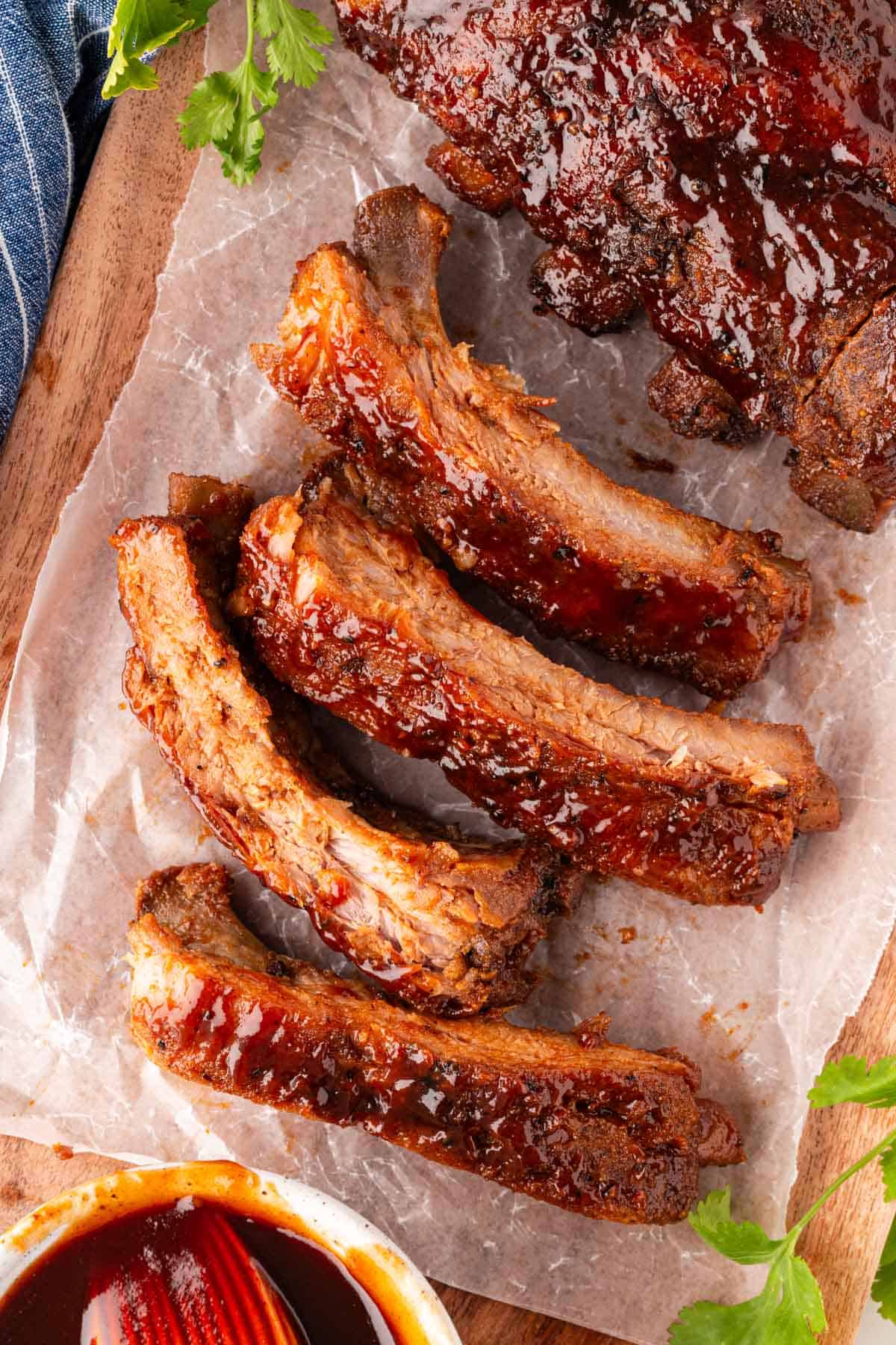 Overhead shot of oven baked ribs sliced and brushed with sauce on parchment paper