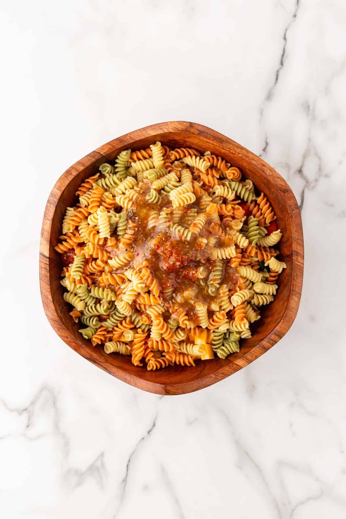 Italian dressing poured over seasoned tricolor rotini pasta in a wooden bowl