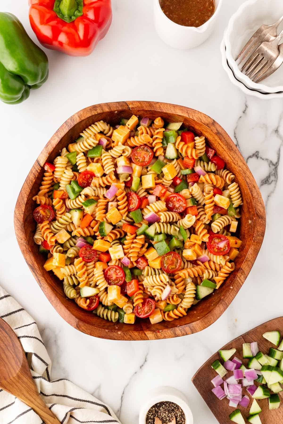 Overhead shot of colorful pasta salad mixed with cheese, cucumbers, tomatoes, peppers, and red onion in a wooden serving bowl