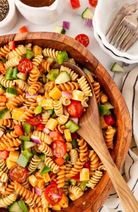 Closeup of colorful pasta salad in a wooden bowl with a wooden serving spoon