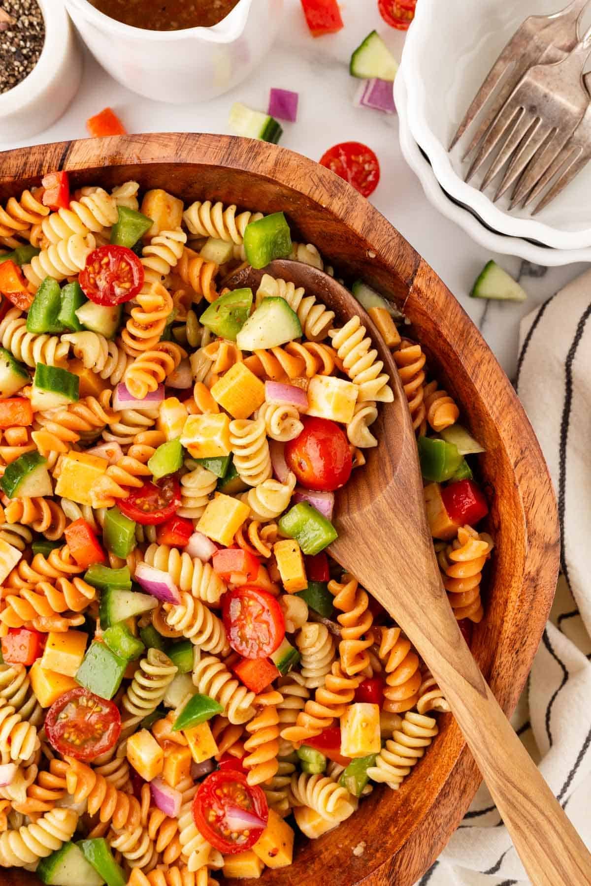 Closeup of colorful pasta salad in a wooden bowl with a wooden serving spoon