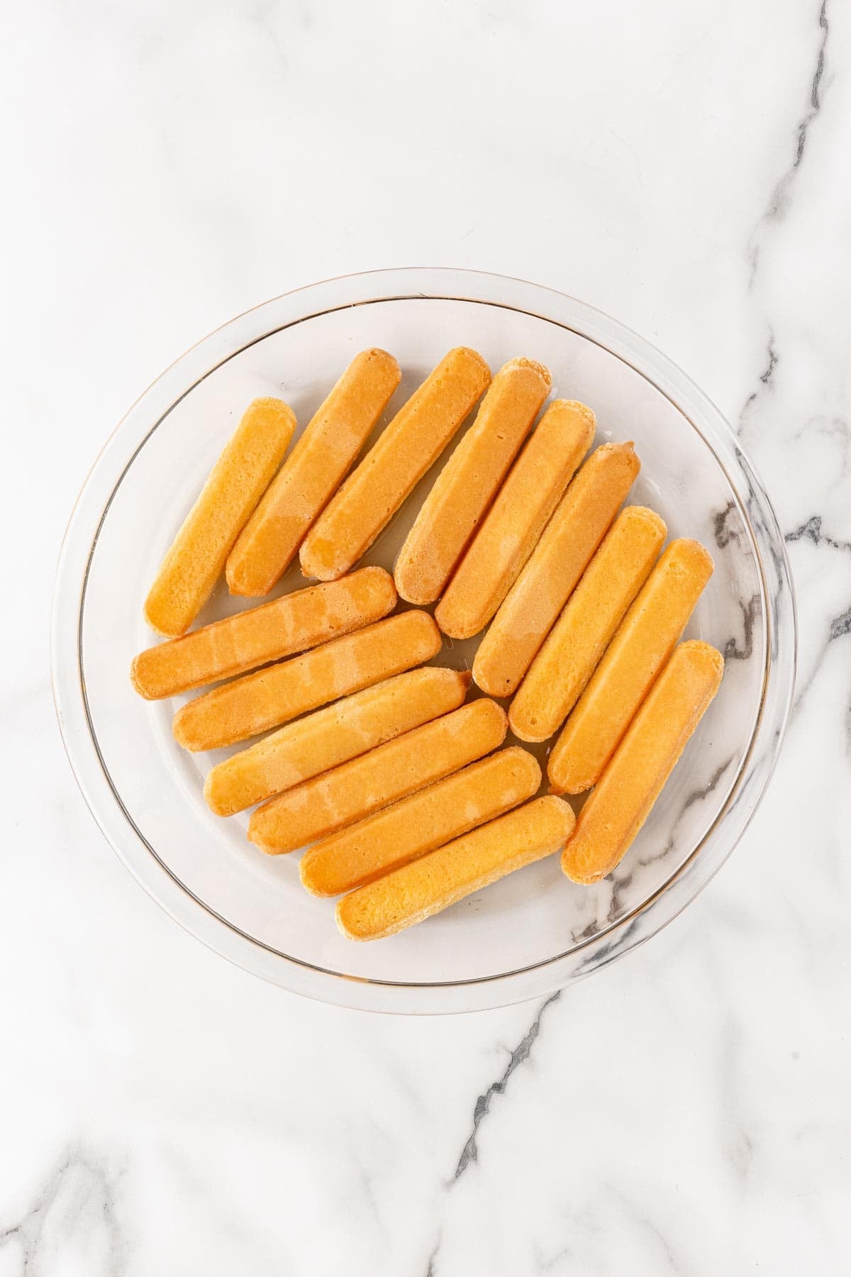Ladyfingers arranged in glass baking dish soaking the peach nectar mixture