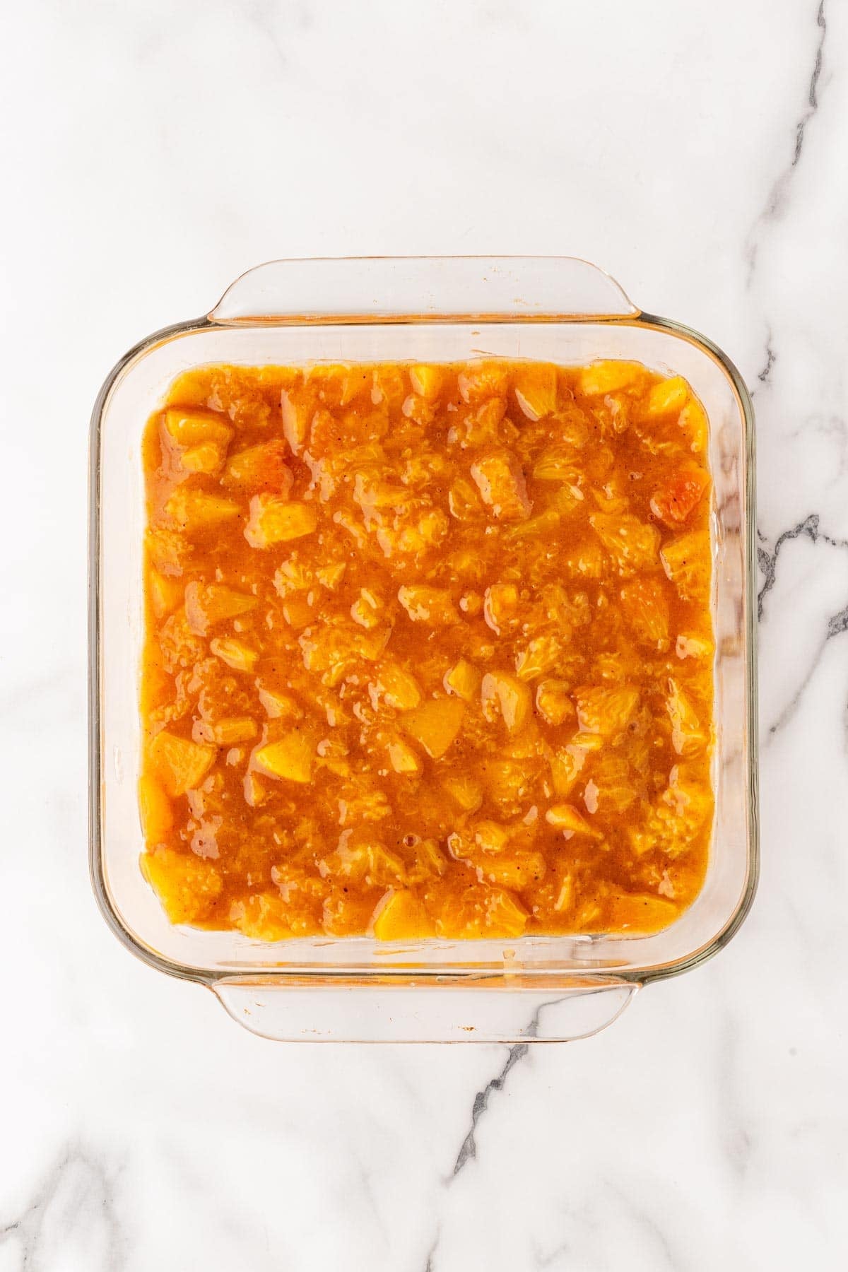 Cooked peach filling spread over cream layer in baking dish