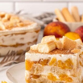 Peach cobbler tiramisu with creamy layers, peaches, and ladyfingers, with more tiramisu and peaches in the background