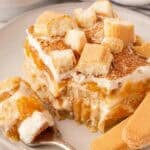 Fork holding a creamy bite of peach cobbler tiramisu beside a layered slice topped with cinnamon and ladyfingers