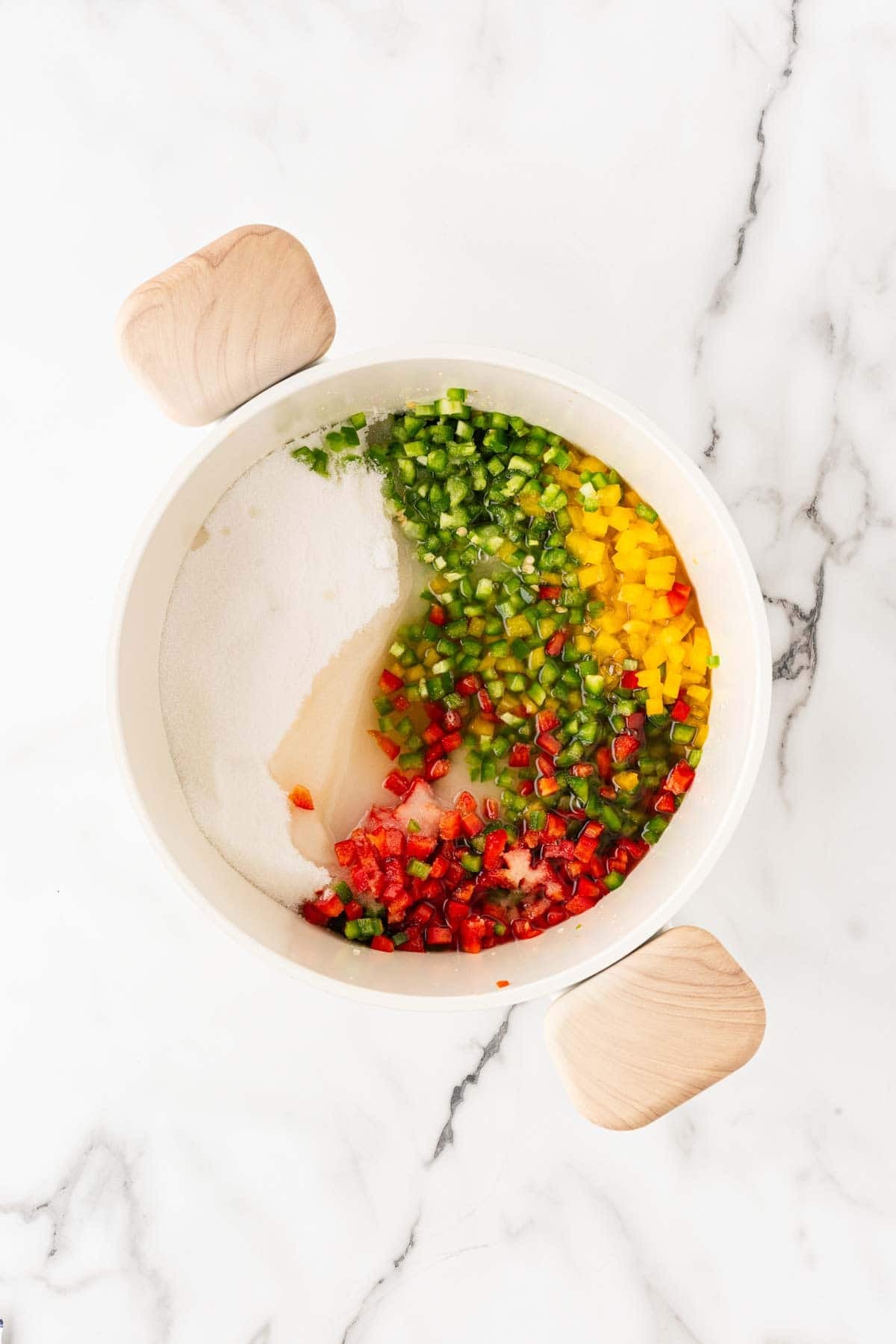 Chopped red, yellow, and green peppers with sugar and liquid in a white pot