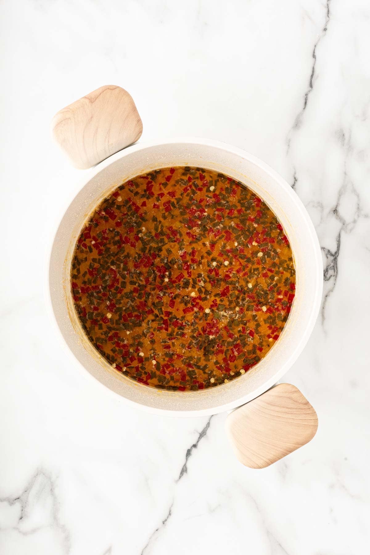 Cooked pepper jelly mixture with diced peppers in a white pot