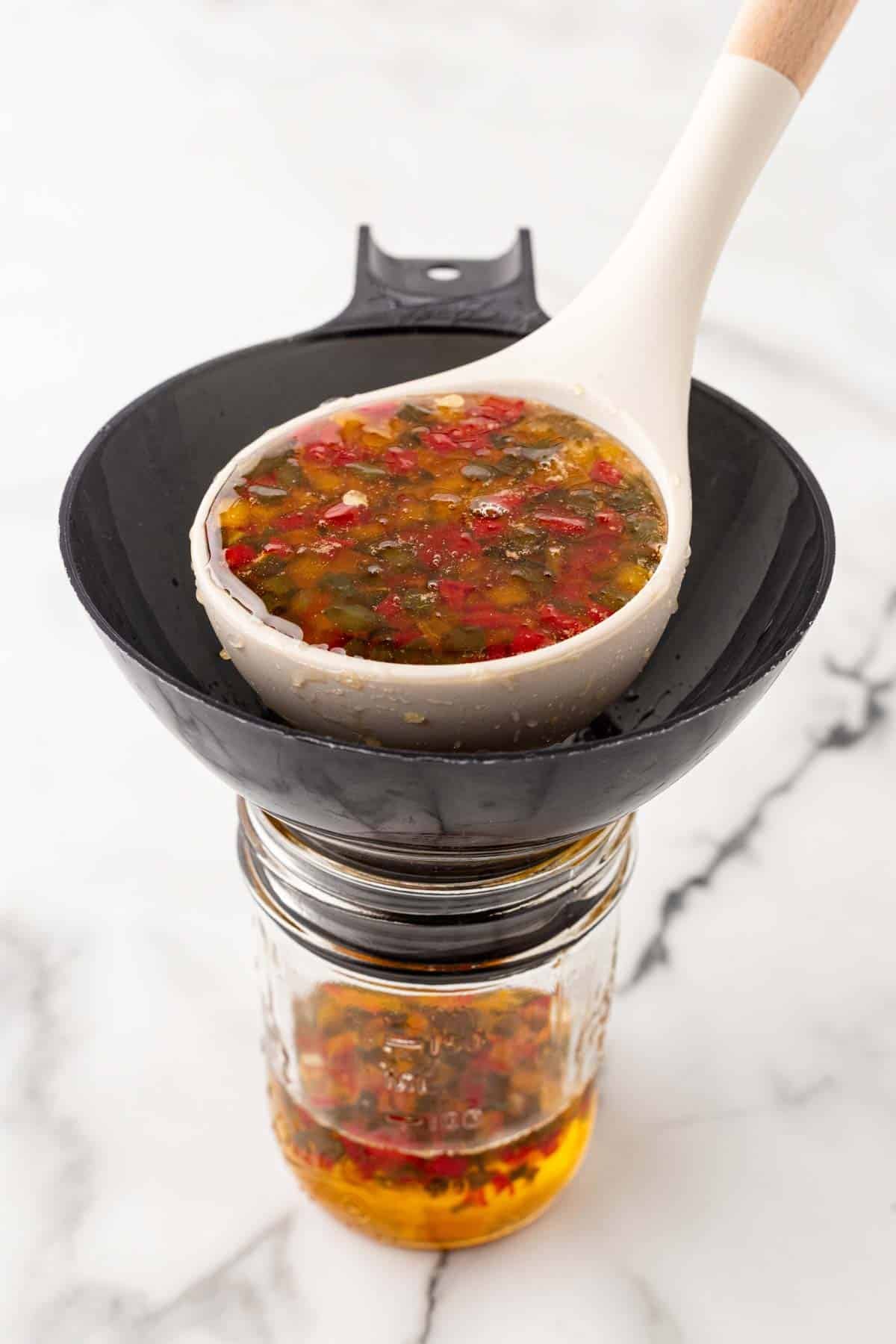 Ladle pouring hot pepper jelly mixture through a funnel into a mason jar