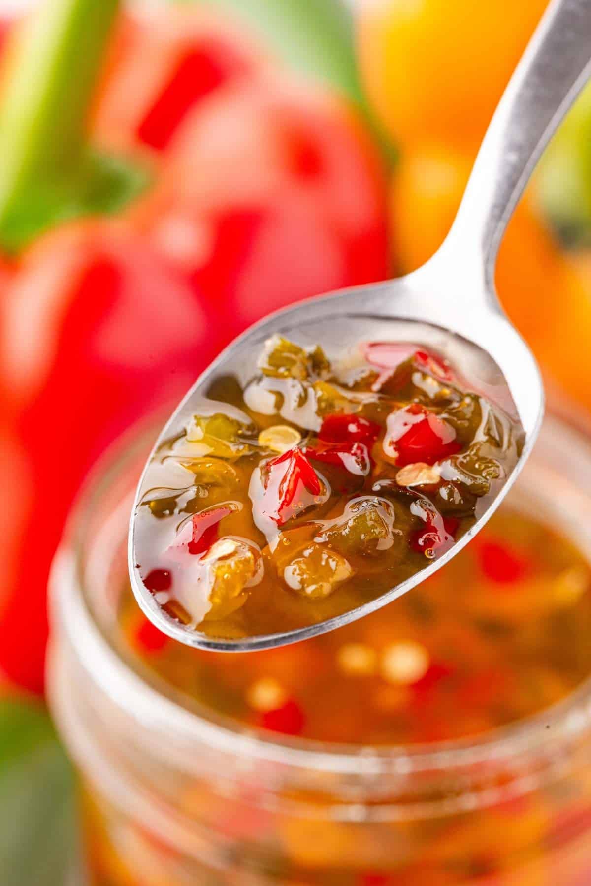 Spoonful of homemade pepper jelly with diced peppers over an open jar