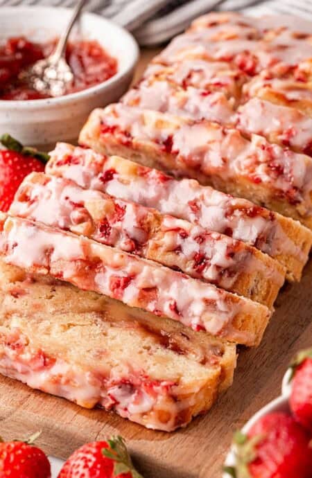 Sliced strawberry bread loaf on wooden board with fresh strawberries
