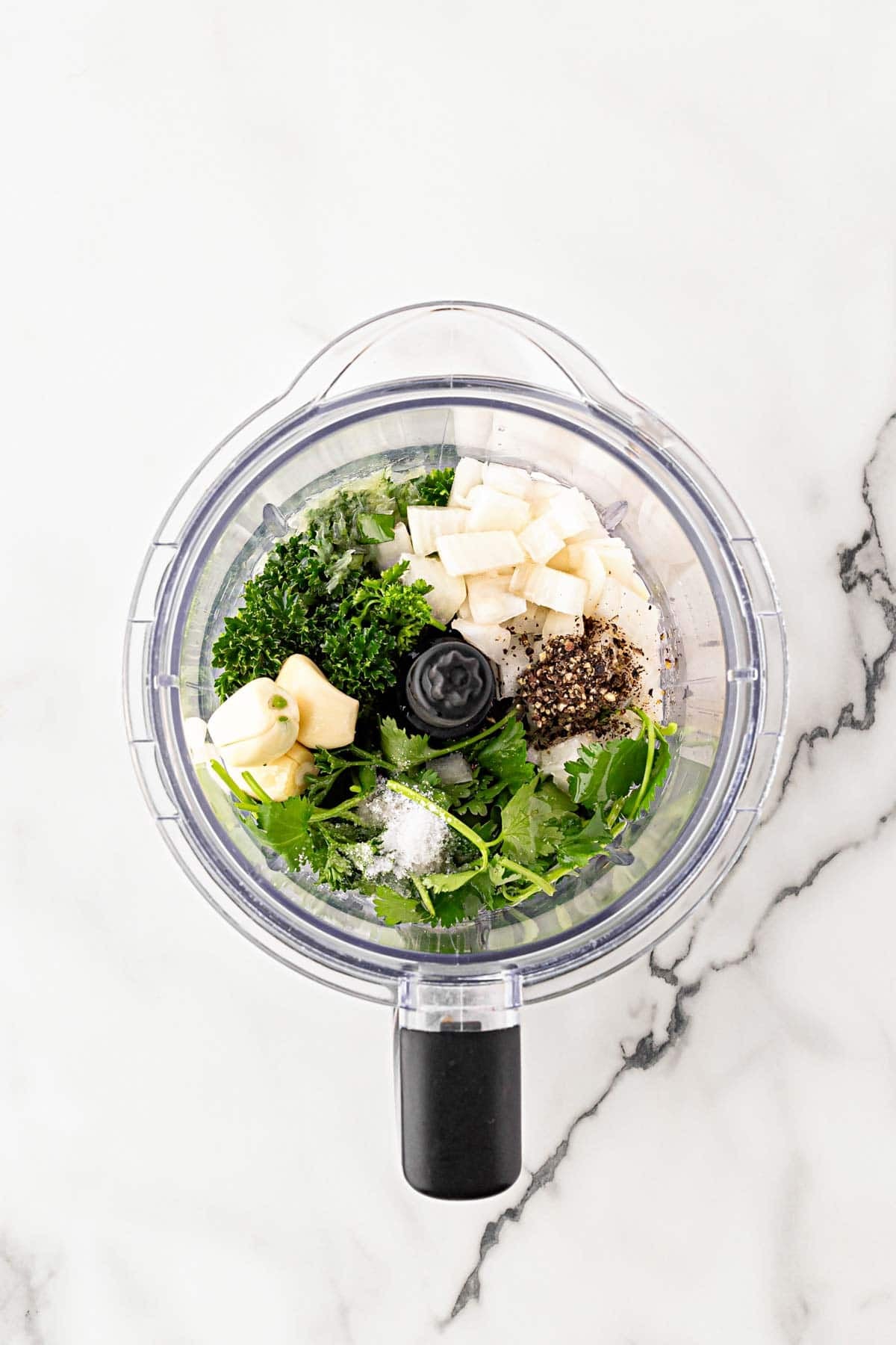 Fresh herbs, garlic, onion, and seasonings added to a food processor for chimichurri sauce