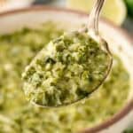 Spoonful of homemade chimichurri sauce lifted from a serving bowl