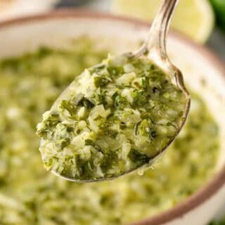 Spoonful of homemade chimichurri sauce lifted from a serving bowl