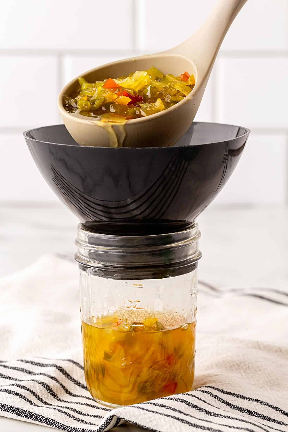Fresh chow chow relish being ladled through a canning funnel into a mason jar