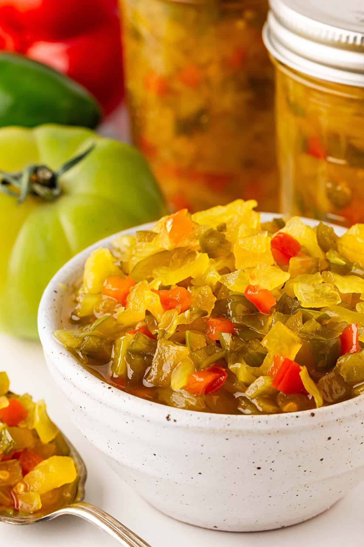 Bowl of homemade chow chow relish with jars and fresh vegetables in the background