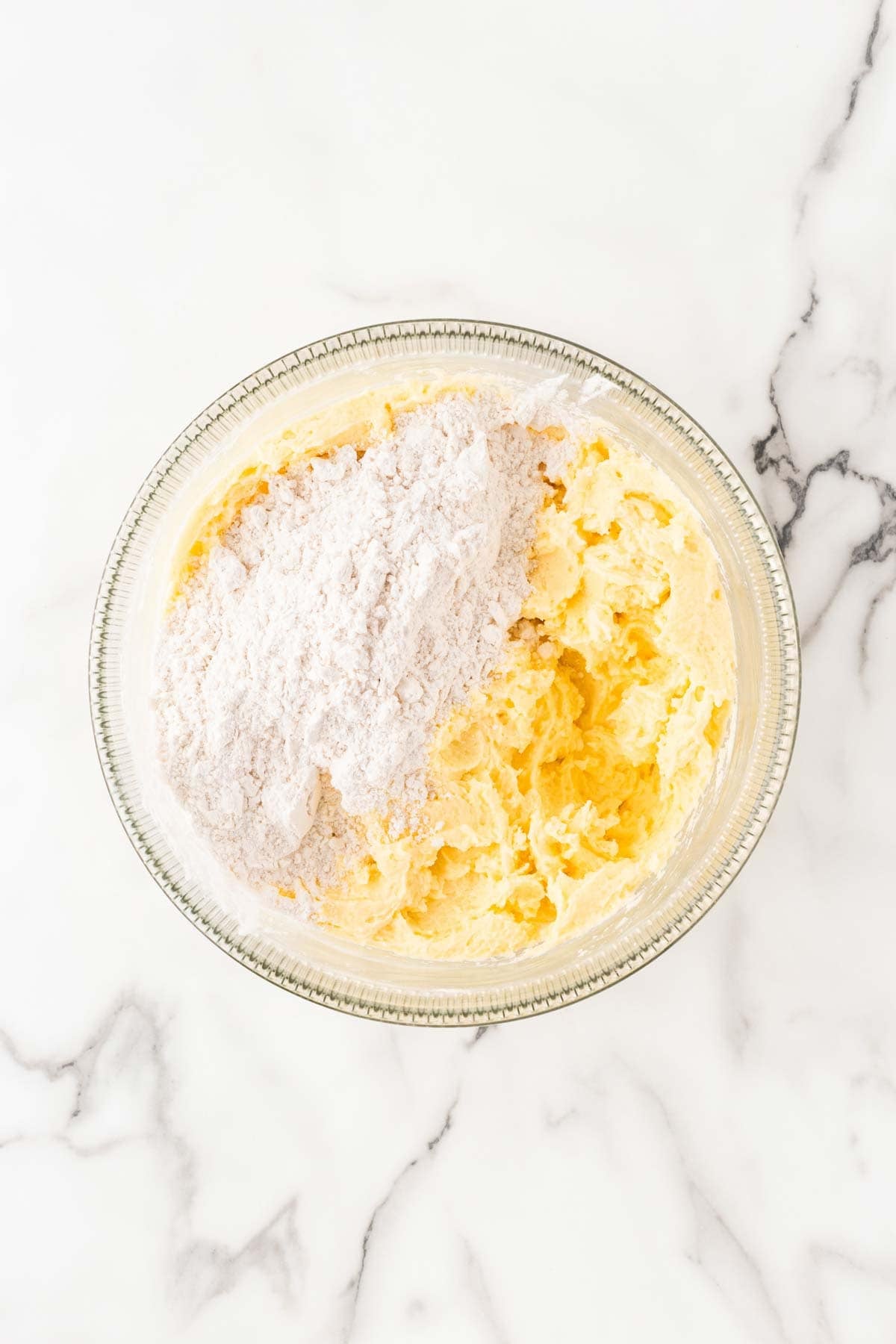 Flour added to the creamed butter mixture in a glass bowl before being mixed into the batter